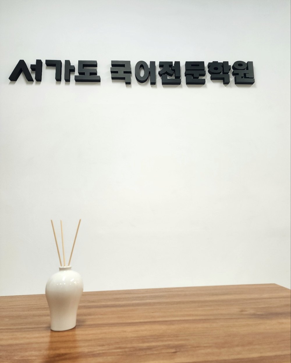 흰 벽의 「서가도 국어전문학원」 입체 사인과 원목 테이블